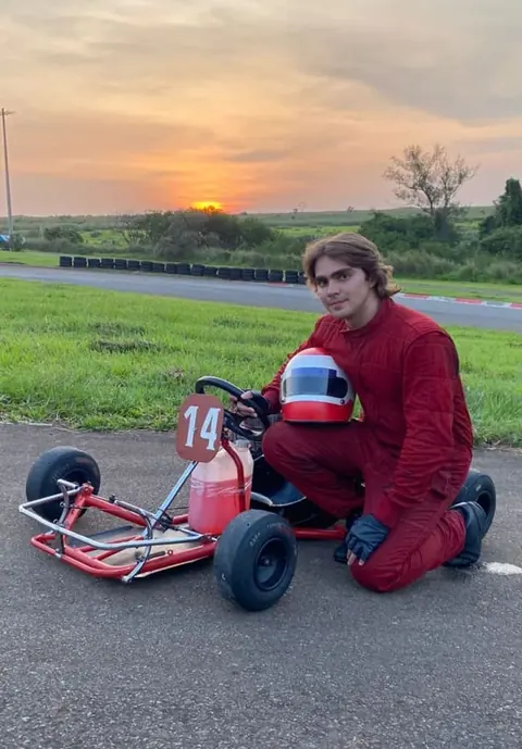 Gabriel caracterizado como Niki Lauda ao lado do kart, ao pôr do sol